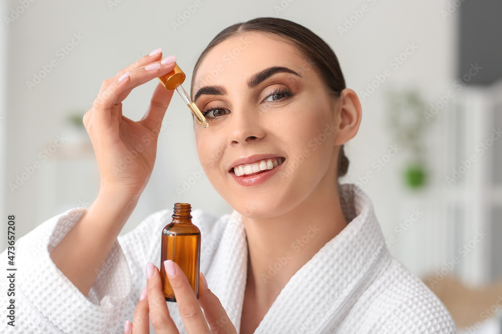 Fototapeta premium Beautiful woman applying essential oil on face in bathroom