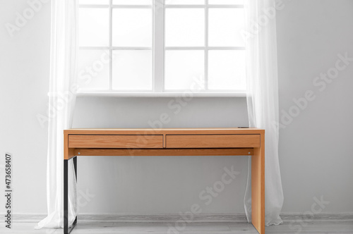 Empty wooden desk near light wall with window