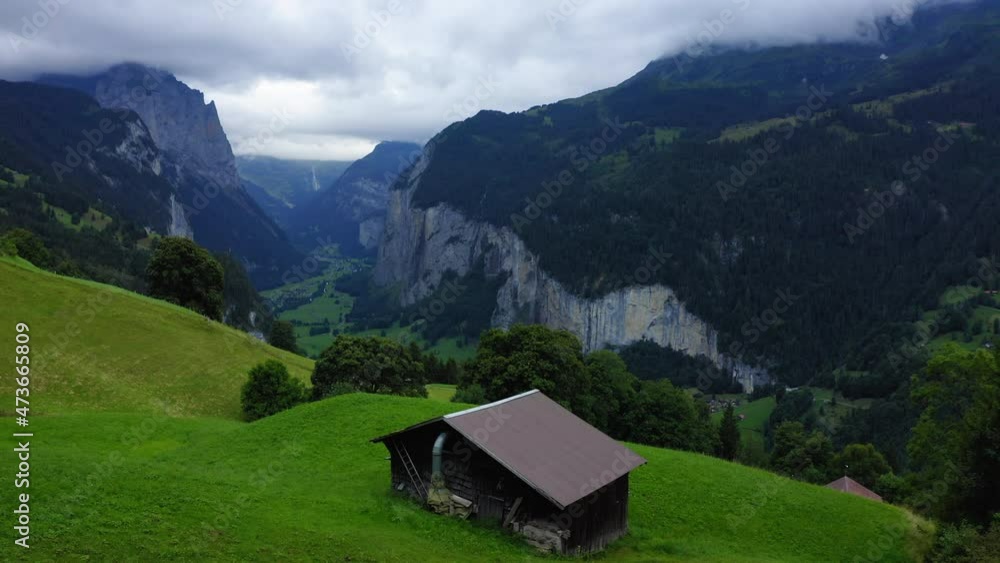 Aerial Forward Beautiful Shot Of Log Cabin On Green Mountain Against Cloudy Sky - Lauterbrunnen, Switzerland Aerial Forward Beautiful Shot Of Log Cabin On Green Mountain Against Cloudy Sky - Lauterbrunnen, Switzerland
