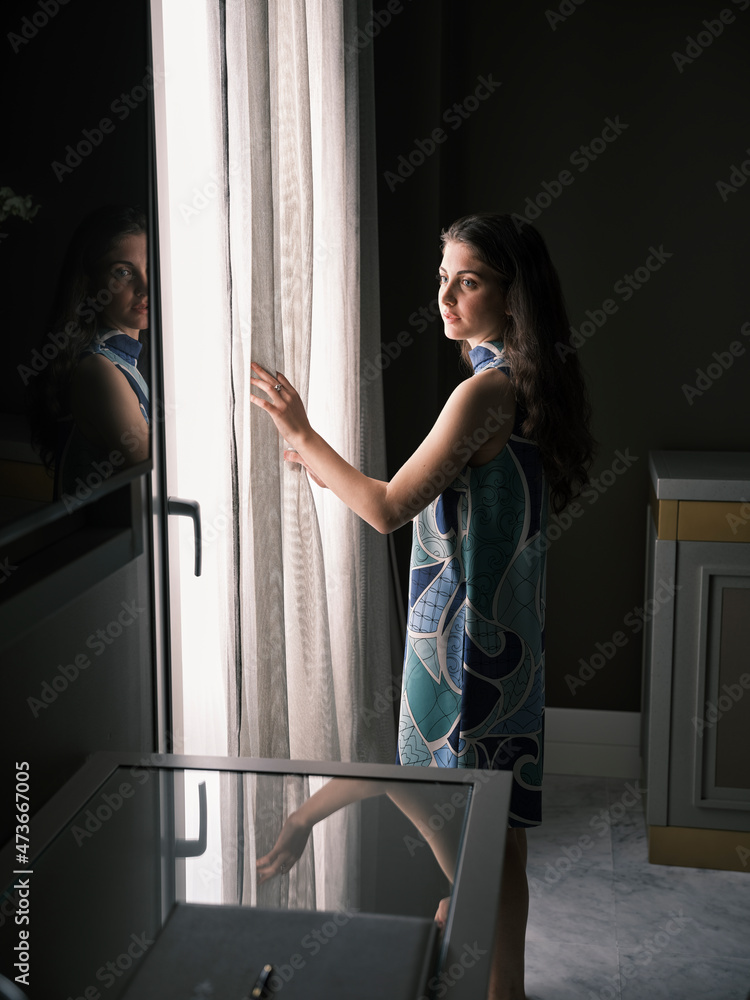 Woman near window opening curtains Woman near window opening curtains