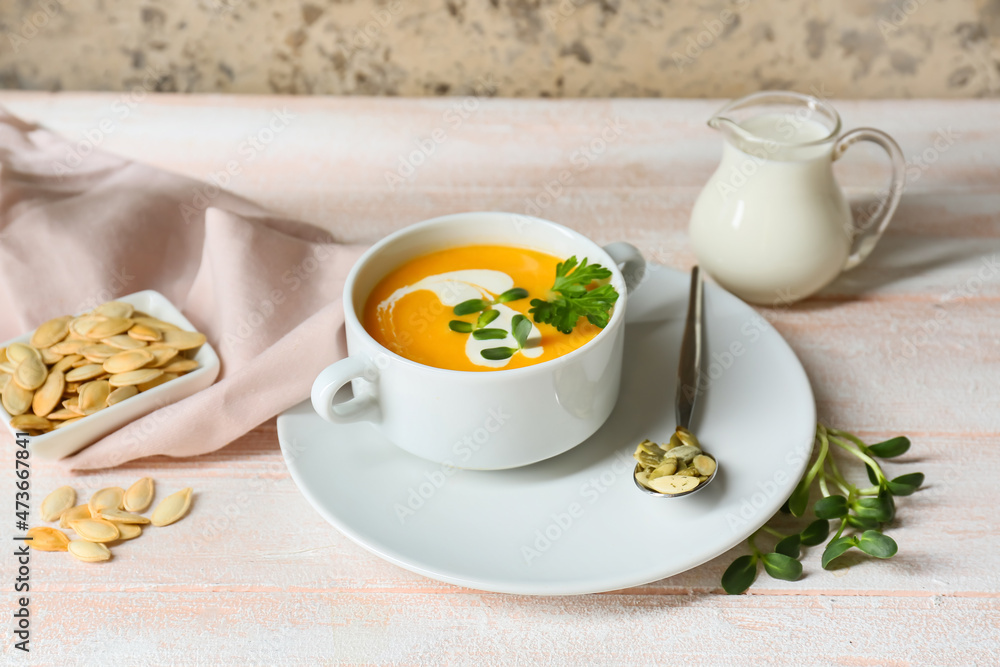 Pot with delicious pumpkin cream soup and seeds on white wooden table