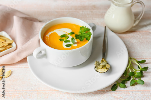 pot with delicious pumpkin cream soup and seeds on white wooden background