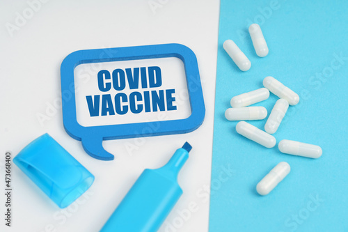 On the white and blue surface are a marker, tablets and a plate inside which the inscription - COVID VACCINE