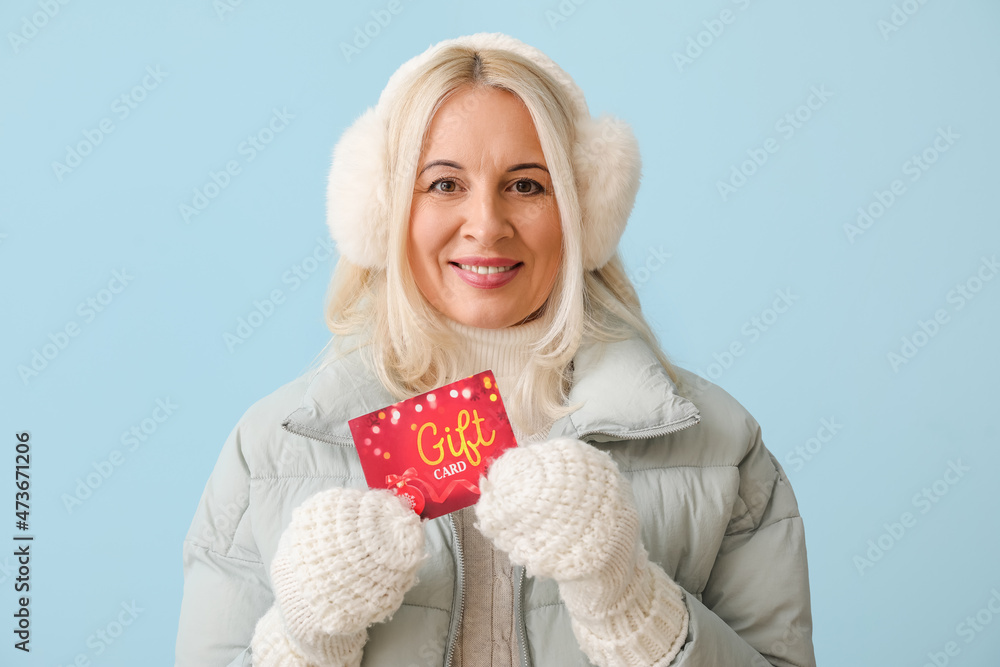 Mature woman in winter clothes and with gift card on color background Mature woman in winter clothes and with gift card on color background
