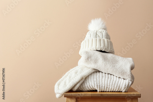 Stylish winter clothes on stool against light background photo