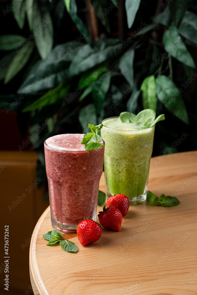 Different smoothies in misted cold glasses, standing on wooden round table, top view, green foliage on blurred background Different smoothies in misted cold glasses, standing on wooden round table, top view, green foliage on blurred background