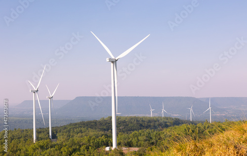 Many wind turbines in rows located with beautiful landscape on the hill with blue sky are operating to generate electric power which is the alternative energy resource for sustainable power supply.