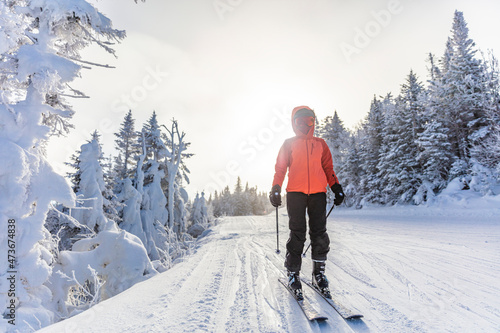 Winter Skiing. Ski woman alpine skier going on skis wearing helmet, cool ski goggles and hardshell winter jacket and ski gloves. Woman going downhill skiing by snow covered trees on ski trail slope