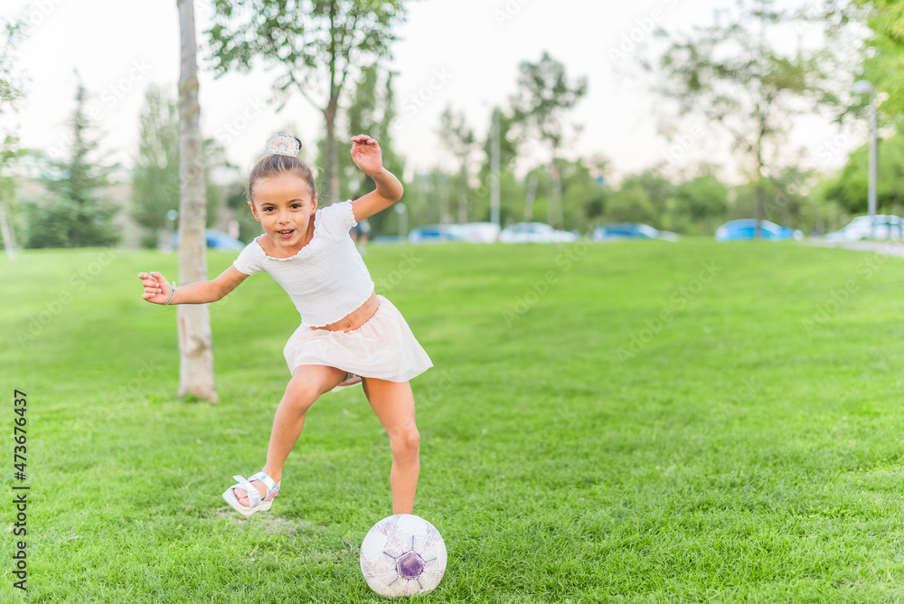 A little girl playing with soccer ball at park