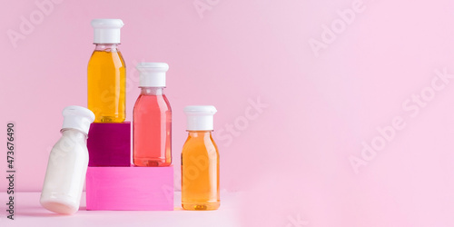  Mockup multicolored plastic bottles with shower gel, shampoo for children and adults on a pink background. Copy space.