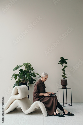 Elegant senior woman using notebook in room with plants photo