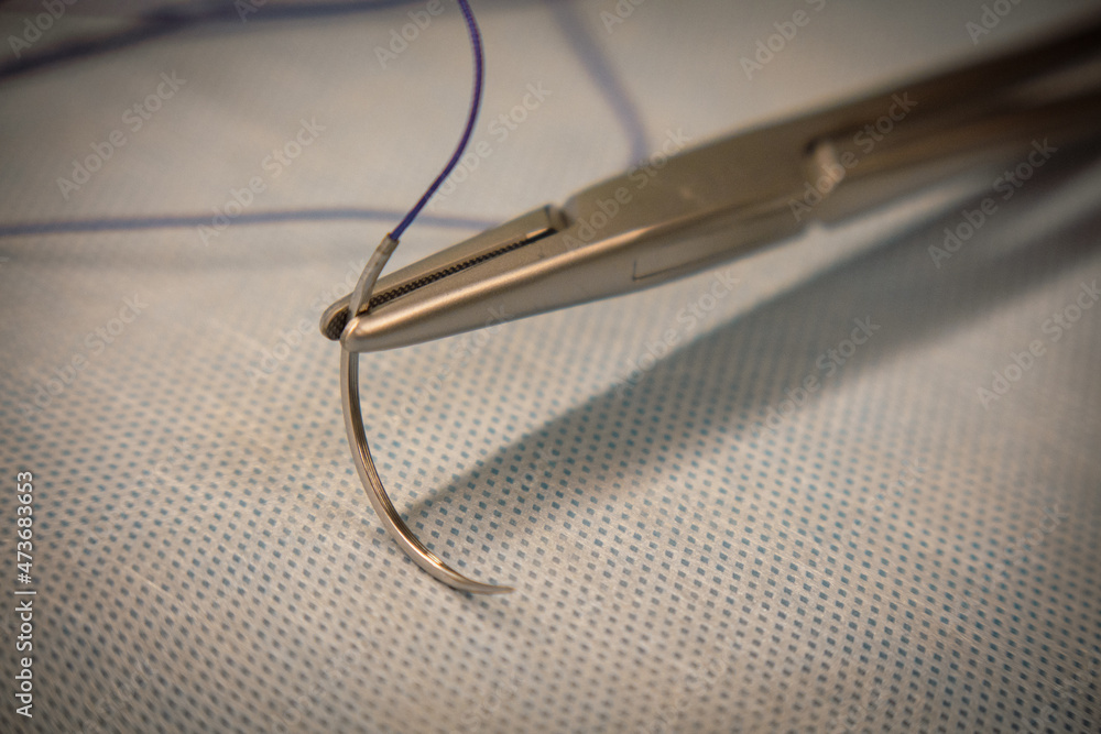 a surgical suture is clamped in a needle holder and a pair of tweezers lies next to it
