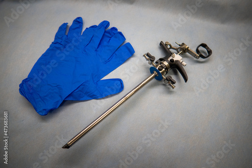 an instrument for performing a prostate resection lies next to blue medical gloves and a glass bulb syringe