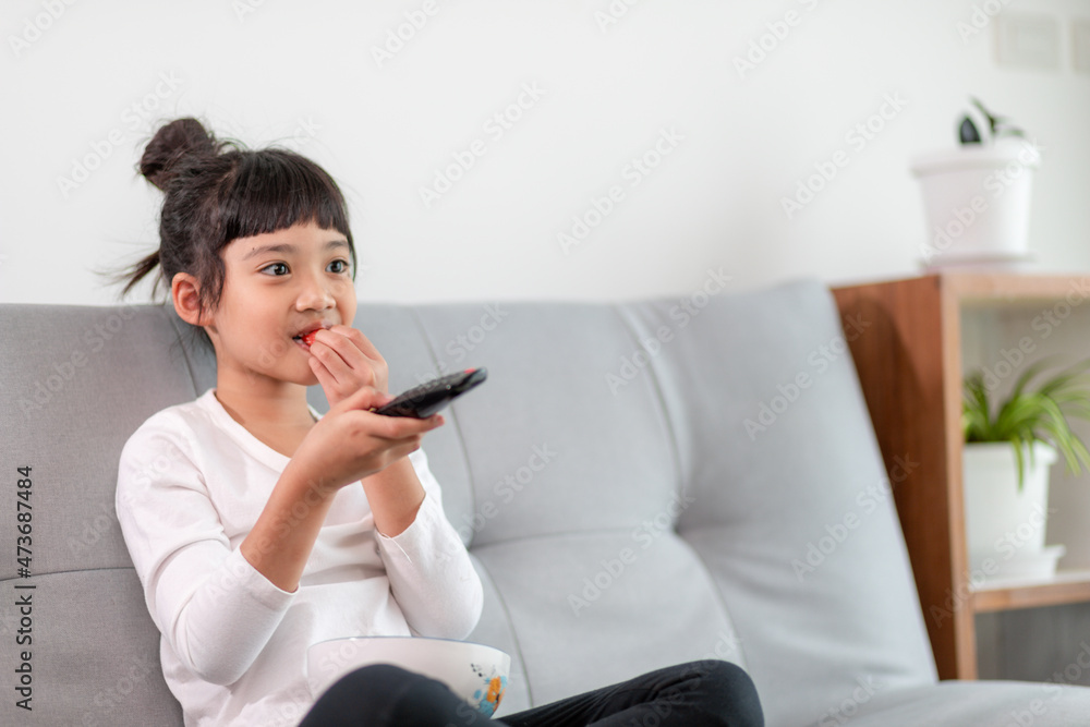 Kid with remote control sitting on the couch watching a movie on tv Kid with remote control sitting on the couch watching a movie on tv