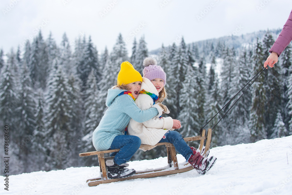 Happy little boy and girl sledding in winter. Kids sibling riding on snow slides in winter. Son and daughter enjoy a sleigh ride. Family christmas holiday outdoor.