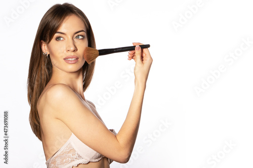 Nude makeup. The girl applies powder to her face with a blush brush.