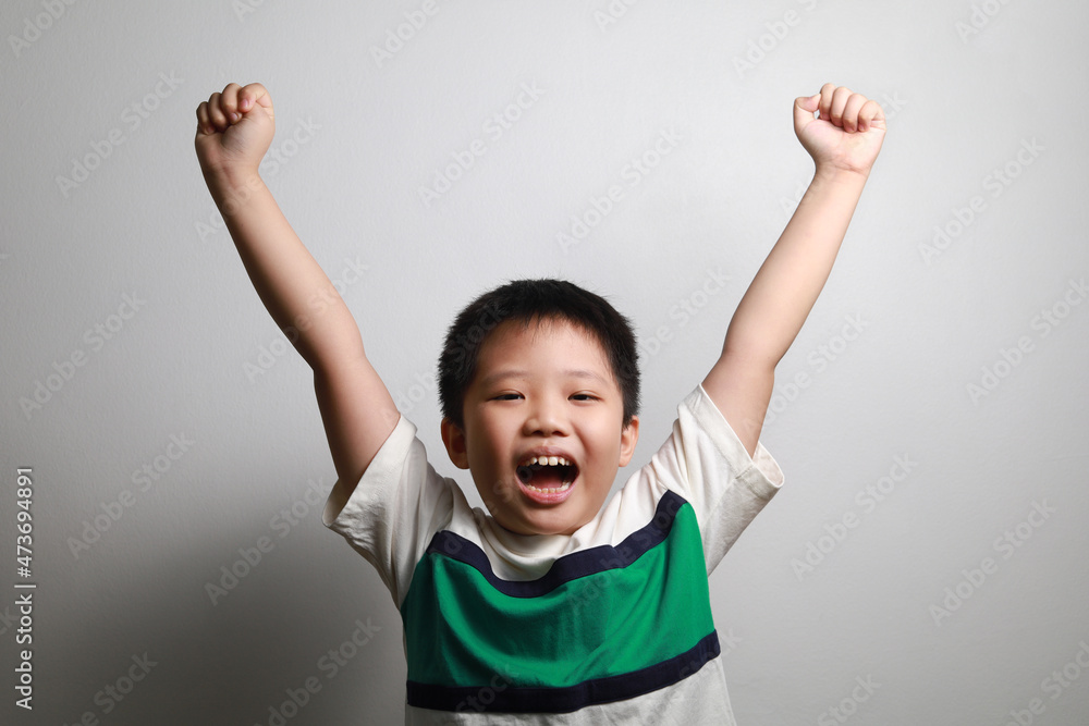 Happy little Asian boy arm rising standing against a grey background Happy little Asian boy arm rising standing against a grey background