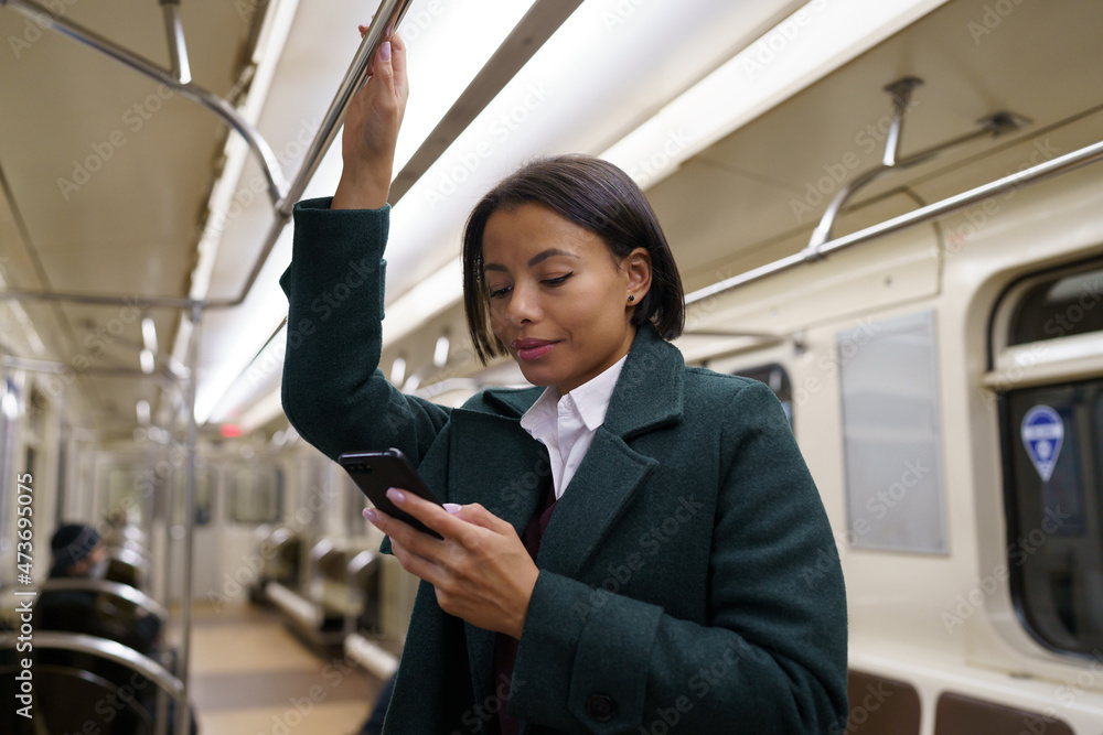 Young afro american woman in metro train using mobile phone, chatting online in social media while returning home after work by public transport. Biracial female suffer from smartphone addiction Young afro american woman in metro train using mobile phone, chatting online in social media while returning home after work by public transport. Biracial female suffer from smartphone addiction