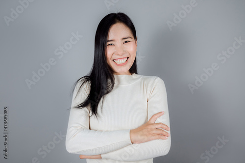 Portrait of smiling Asian woman wears cream sweater standing on gray background