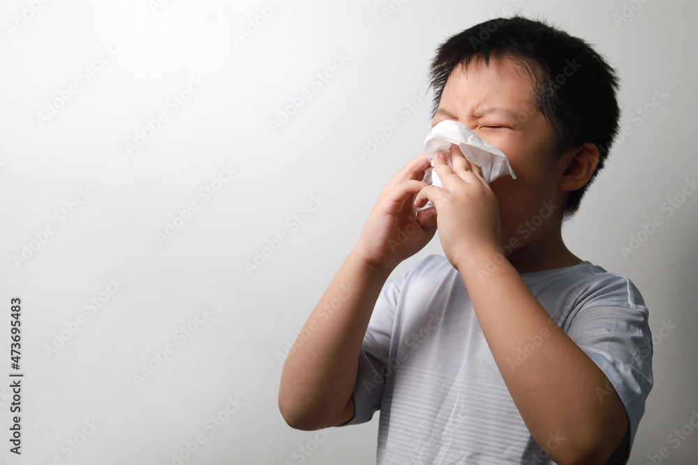 Cropped shot of an adorable little boy blowing his nose while standing against a white wall. Copy space. Cropped shot of an adorable little boy blowing his nose while standing against a white wall. Copy space.