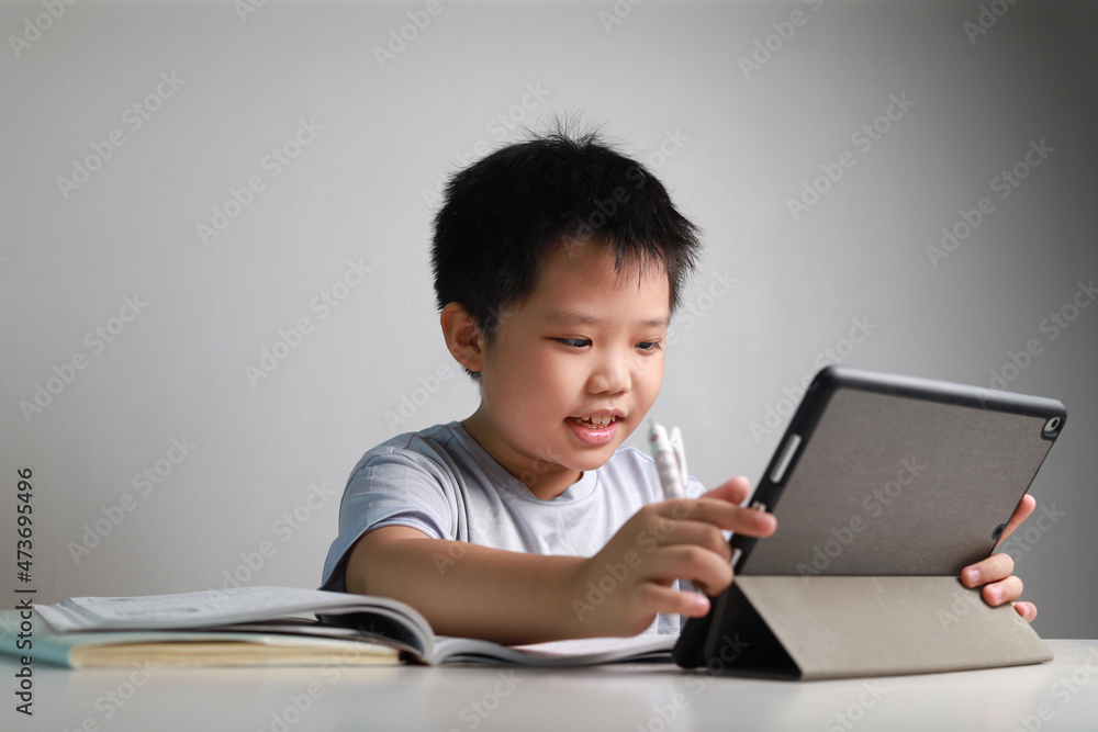 Portrait of a little Asian boy using tablet computer and headphone during pandemic lockdown, homeschooling, social distance, stay at home, online education concept. Portrait of a little Asian boy using tablet computer and headphone during pandemic lockdown, homeschooling, social distance, stay at home, online education concept.