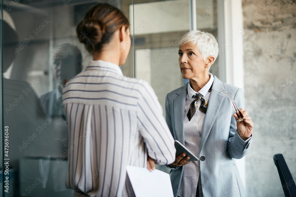 Senior businesswoman talks to female colleague while working at corporate office.