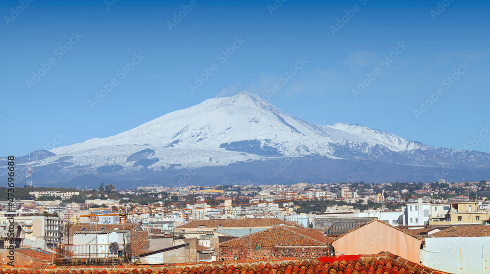 Panoramic view over Catania with the snowy volcano Etna behind city houses. Focus on roofs