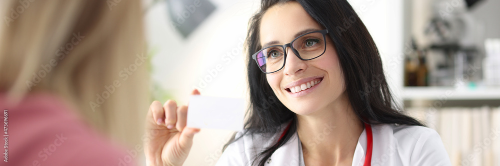 Woman doctor holds out business card to patient Woman doctor holds out business card to patient