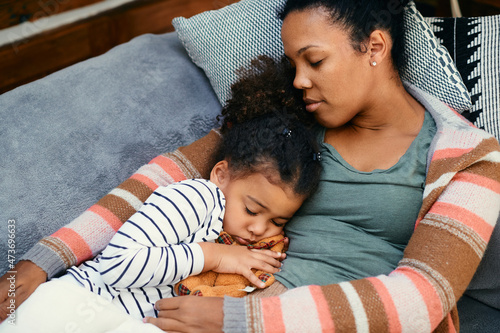 Loving black mother and daughter napping together on sofa at home.