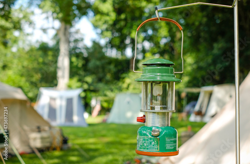 Close up Beautiful vintage camping lantern hanging on a steelstand with a background of tents in the camping,Relaxing in the midst of nature