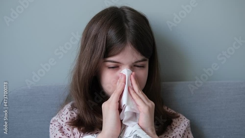 Little girl, a teenager is sick with the flu, blows her nose in a napkin