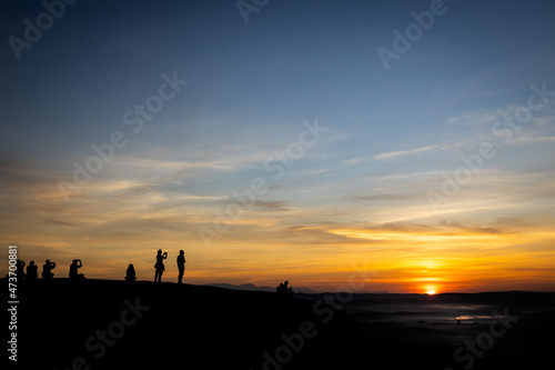 Silhouette picture of tourists taking photos with the rising sun,people watch the first light and the morning mist,sunrise in the morning at Three Whale Rocks in Phu Sing National forest,Bueng Kan © Satjawat