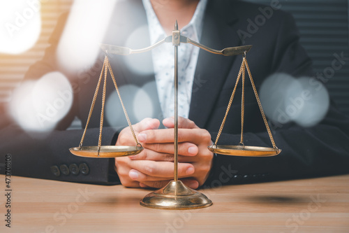 Male lawyer in the office with brass scale on wooden table, justice and law concept.