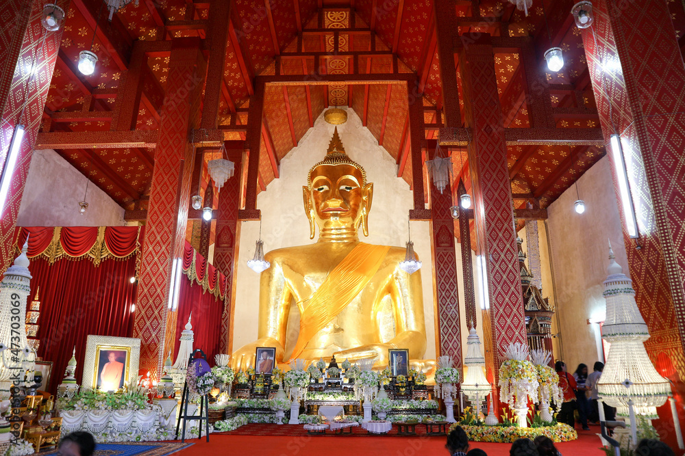 The Buddha statue is placed in a large temple room. Inside there is a beautiful pattern in gold and red.