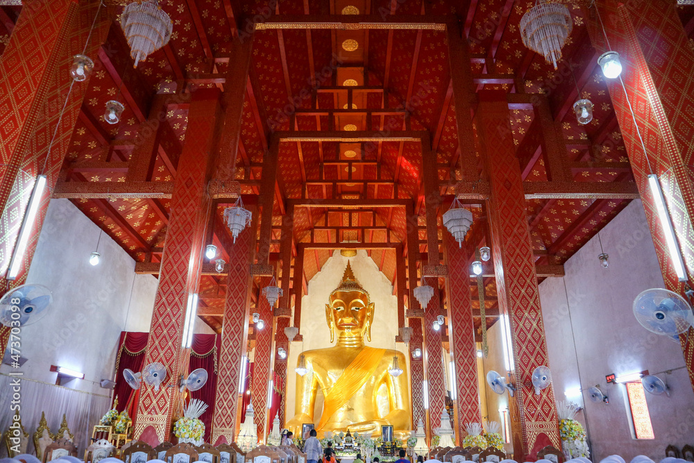 The Buddha statue is placed in a large temple room. Inside there is a beautiful pattern in gold and red.