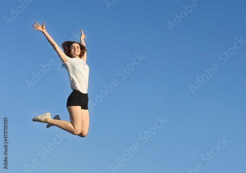 Positive sport girl on background of blue sky. Slender woman jumping. Keep fit