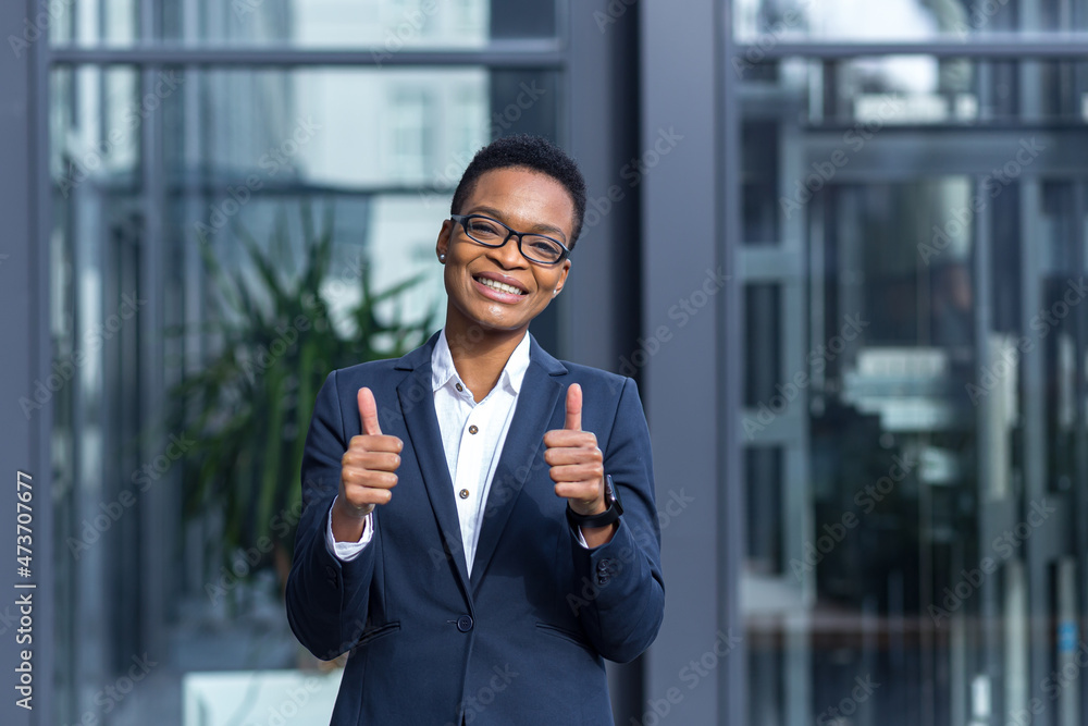 Portrait of young successful business woman, african american woman smiling happy looking at camera, wearing glasses, near modern office Portrait of young successful business woman, african american woman smiling happy looking at camera, wearing glasses, near modern office
