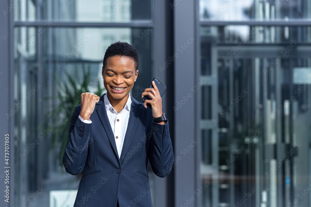 Beautiful and joyful woman with short hair African American student, rejoices in the news reads from the phone the good news, smiles Beautiful and joyful woman with short hair African American student, rejoices in the news reads from the phone the good news, smiles