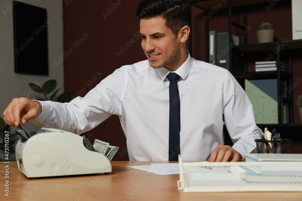 Man putting money into banknote counter at wooden table indoors Man putting money into banknote counter at wooden table indoors