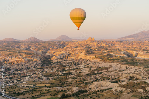 Cappadocia, Turkey - 21 July 2021: Colorful hot air balloon flying over white mountains in sunrise sky. Goreme mountains scenic view