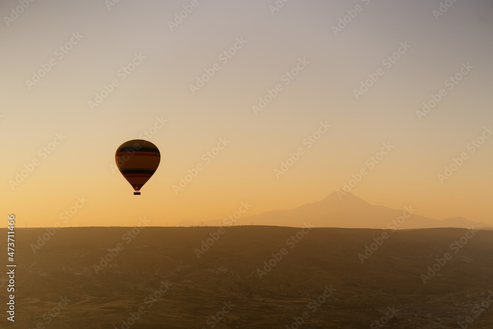 Obraz premium Cappadocia, Turkey - 21 July 2021: Colorful hot air balloon flying over white mountains in sunrise sky. Goreme mountains scenic view
