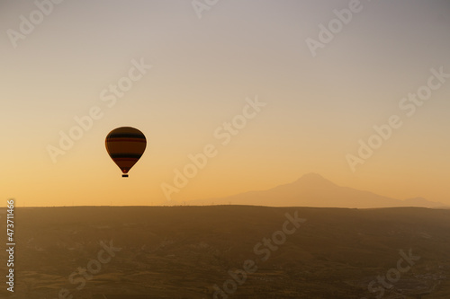 Cappadocia, Turkey - 21 July 2021: Colorful hot air balloon flying over white mountains in sunrise sky. Goreme mountains scenic view