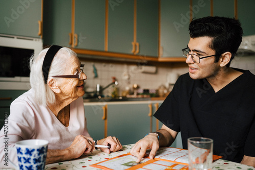 Smiling senior woman talking with male nurse in kitchen at home photo