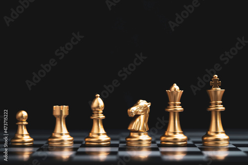 Golden chess include king queen horse ship and pawn on dark background.