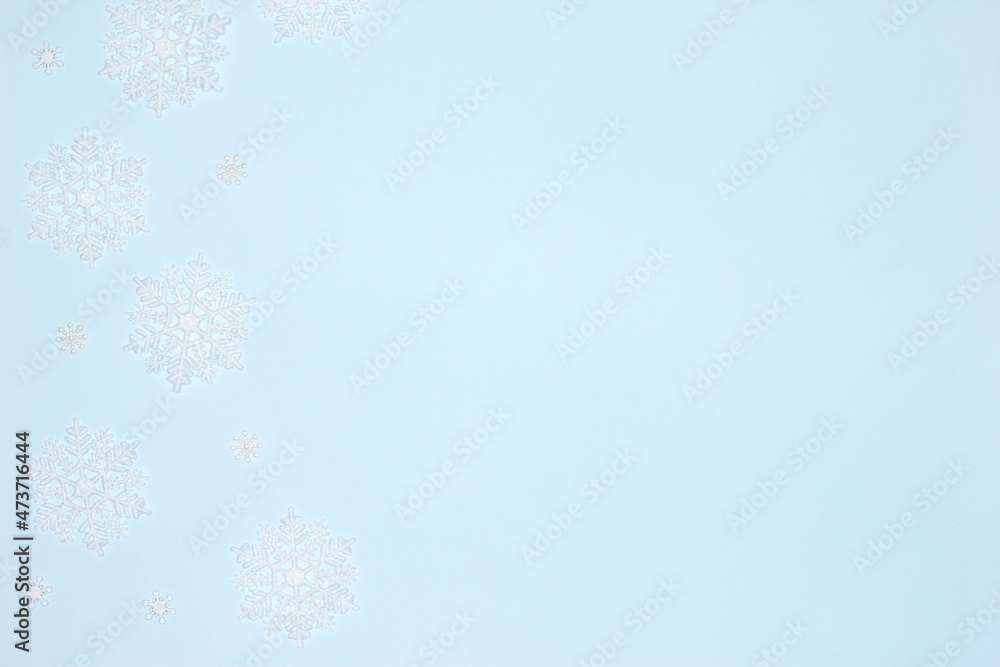 White luminous snowflake decorations frame flat lay on pastel blue background. Copy space. Simple winter backdrop