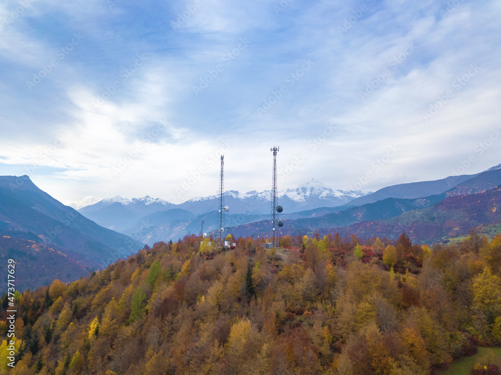 Drone view of two high-voltage towers with antennas in the forest in the mountains on an autumn day.