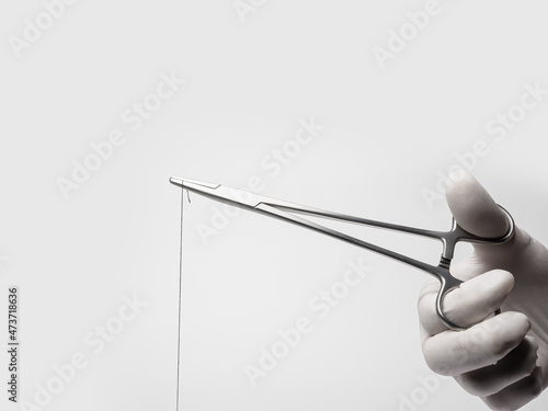 Hand in latex glove holding surgery or suture clamp on white background photo