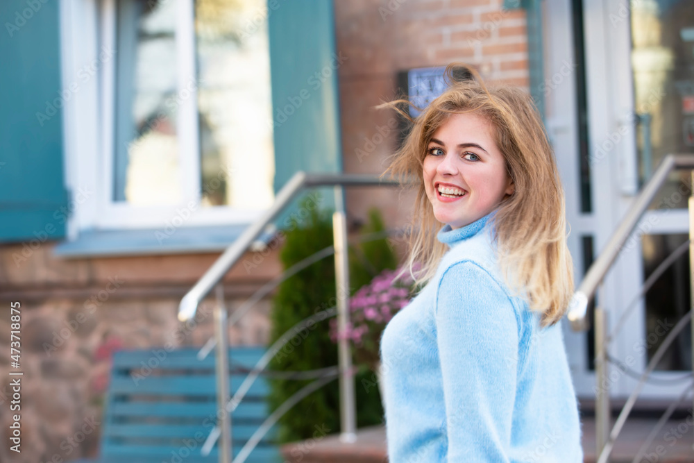 On the street, a happy blonde girl in a blue knitted sweater.