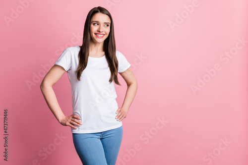 Portrait of attractive cheerful girl hands on hips looking aside copy blank space isolated over pink pastel color background © deagreez
