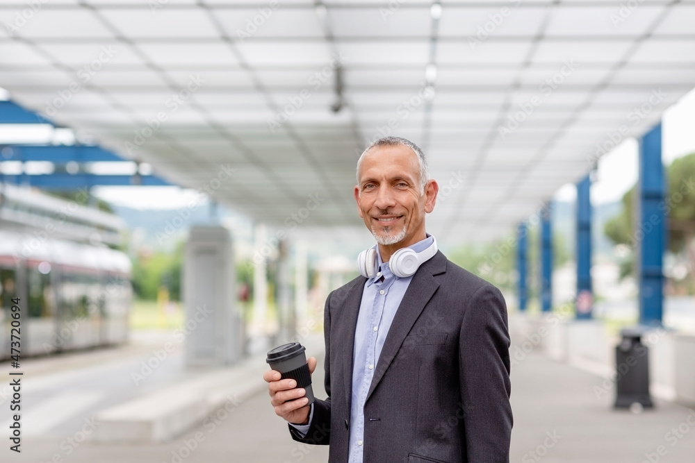 Smiling businessman holding reusable cup at railroad station Smiling businessman holding reusable cup at railroad station
